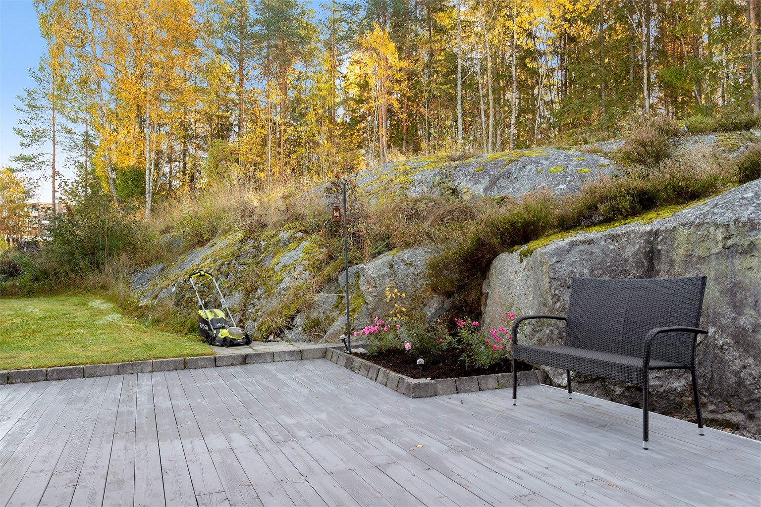 Terrasseplattingen glir over i plen og beplantede bed langs fjellveggen.