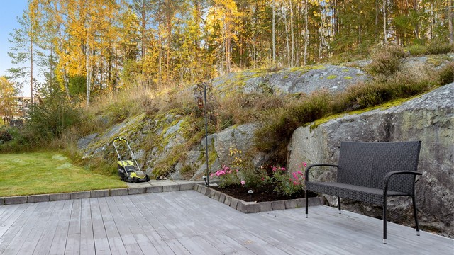 Terrasseplattingen glir over i plen og beplantede bed langs fjellveggen.