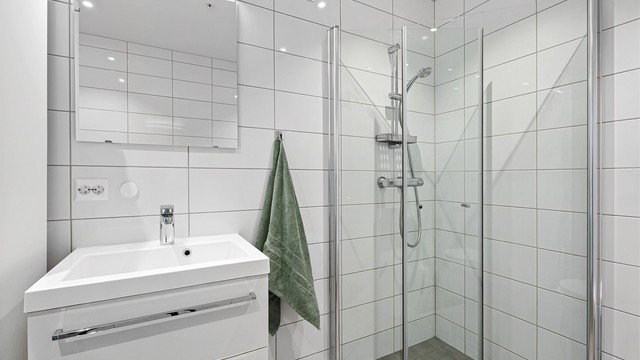 Badet har dusjnisje med innfellbare dører, vegghengt servant med skuffer samt speil med belysning.