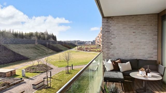 Balkongen er belagt med terrassebord og har rekkverk i metall og glass.