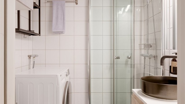 Videre har badet gulvstående toalett og dusjhjørne med glassdører og to-greps armatur samt regnfalldusj. Det er opplegg for vaskemaskin.