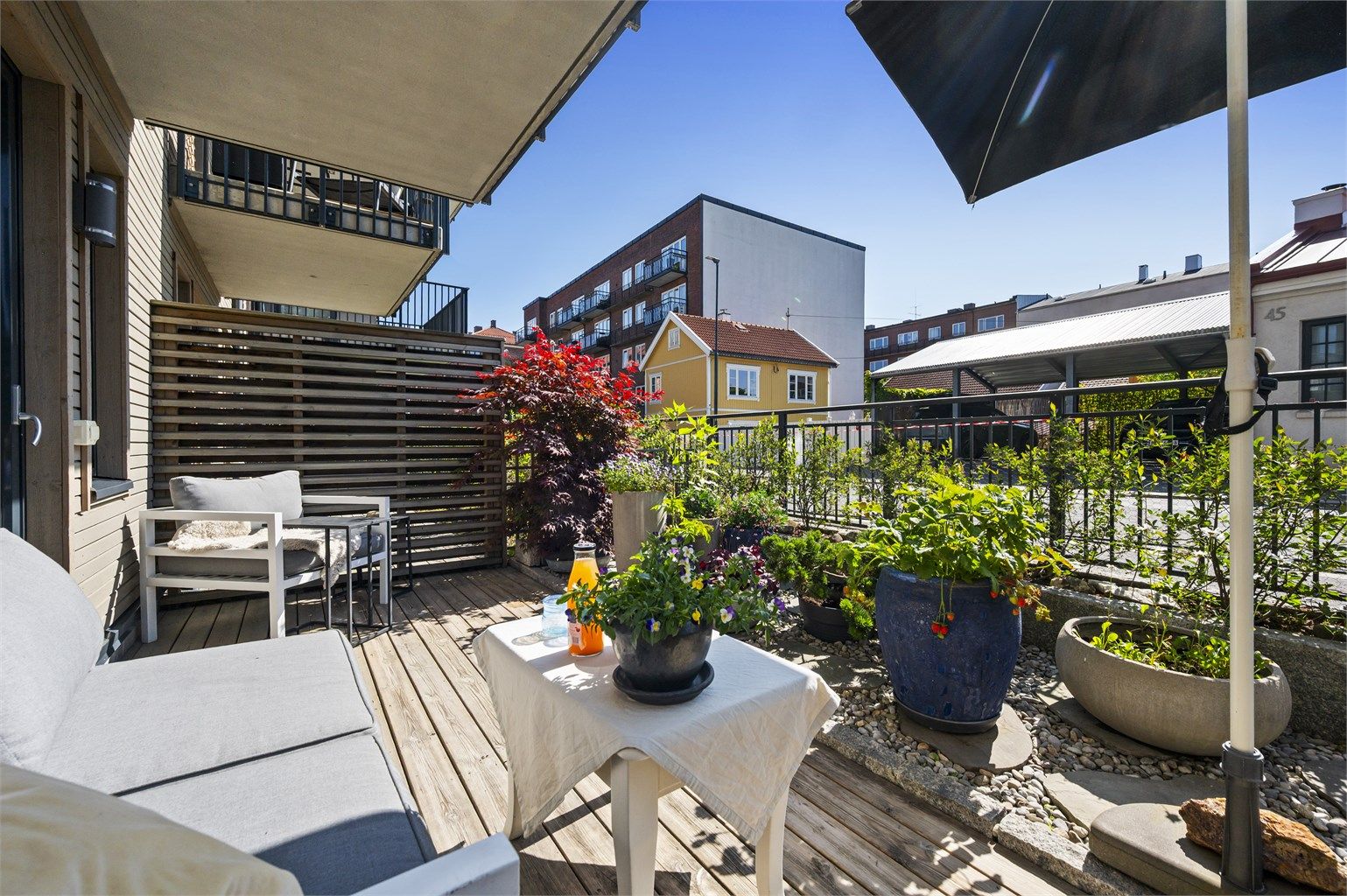 Terrassen mot rolige Fjellgata er en idyllisk oase med nydelig utsikt over hyggelig trehusbebyggelse. Plass til sittegrupper, planter og grill. Her er det sol fra morgen til ca 15.30.