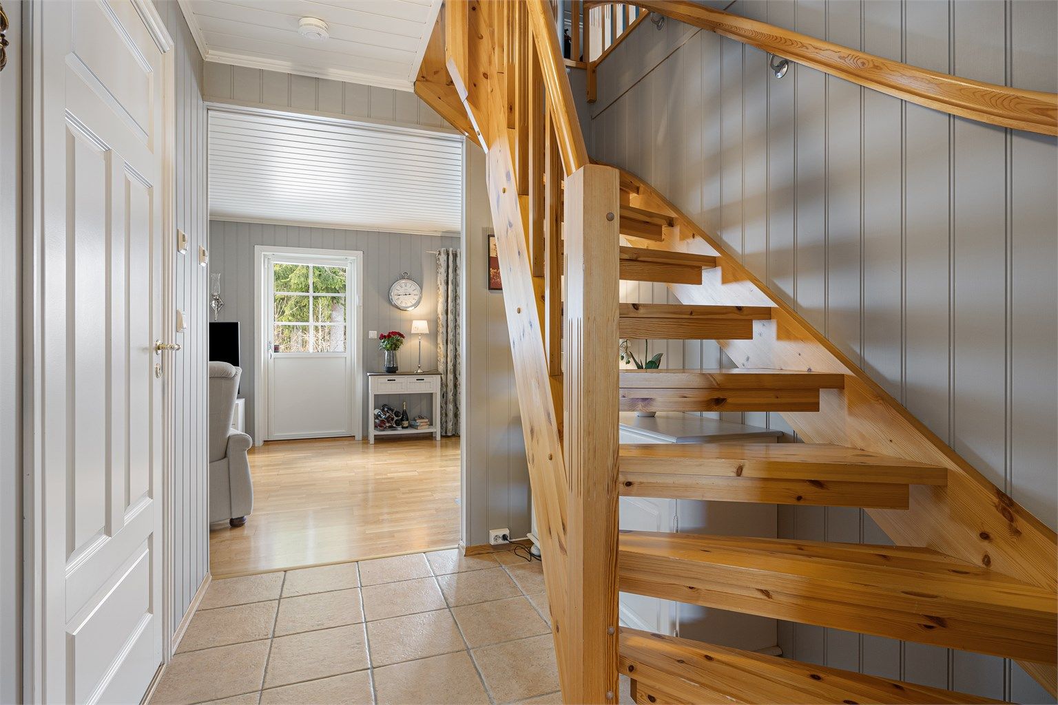 Innvendig trapp i treverk med åpne opptrinn leder opp til loftsetasjen.