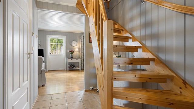 Innvendig trapp i treverk med åpne opptrinn leder opp til loftsetasjen.