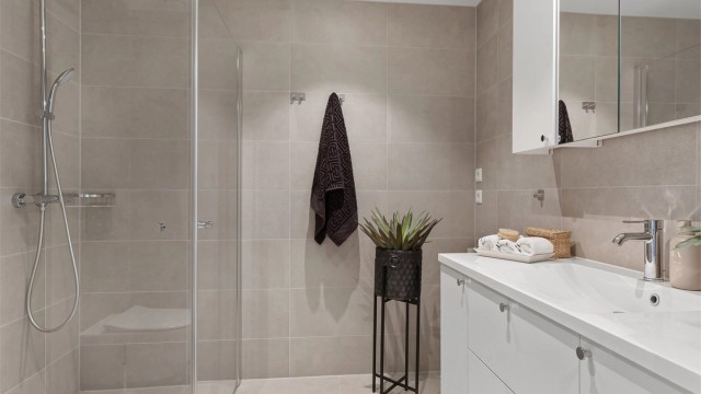 Lekkert baderom med fliser på gulv, fliser på vegger og malt himling med downlights