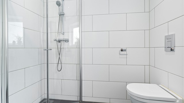 Dusjhjørnet har plassbesparende, foldbare dører og stilren armatur. Videre er det veggmontert toalett, opplegg for både vaskemaskin og tørketrommel, samt mekanisk avtrekk fra badet