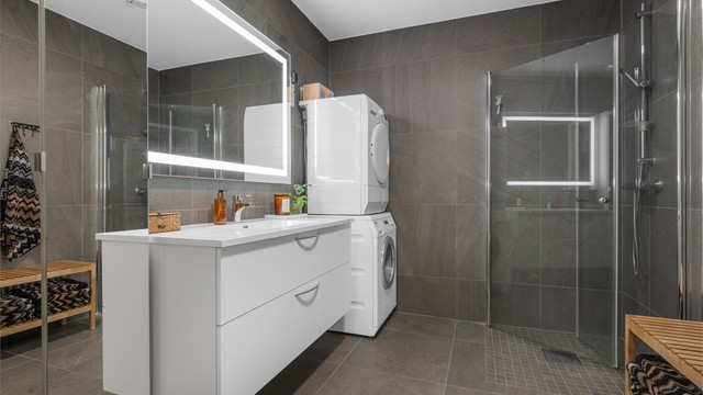 Videre er badet innredet med servantskap med speil og lys, sideskap og dusjhjørne.