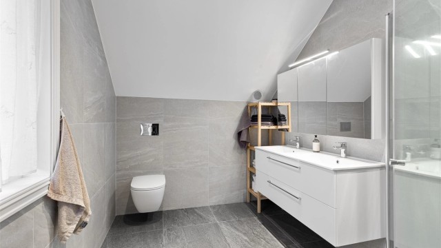 Flott flislagt bad 2 fra 2023 med adkomst fra hovedsoverommet. Downlights i himlingen. Innredet med vegghengt servantinnredning med skuffer. Speilskap med overlys over servant. Foto: Ole Thorgeir Solheim Thoresen