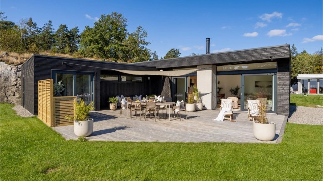 Arkitekttegnet funkis-hytte i L-form, designet for å omfavne uterommet og sjøutsikten.