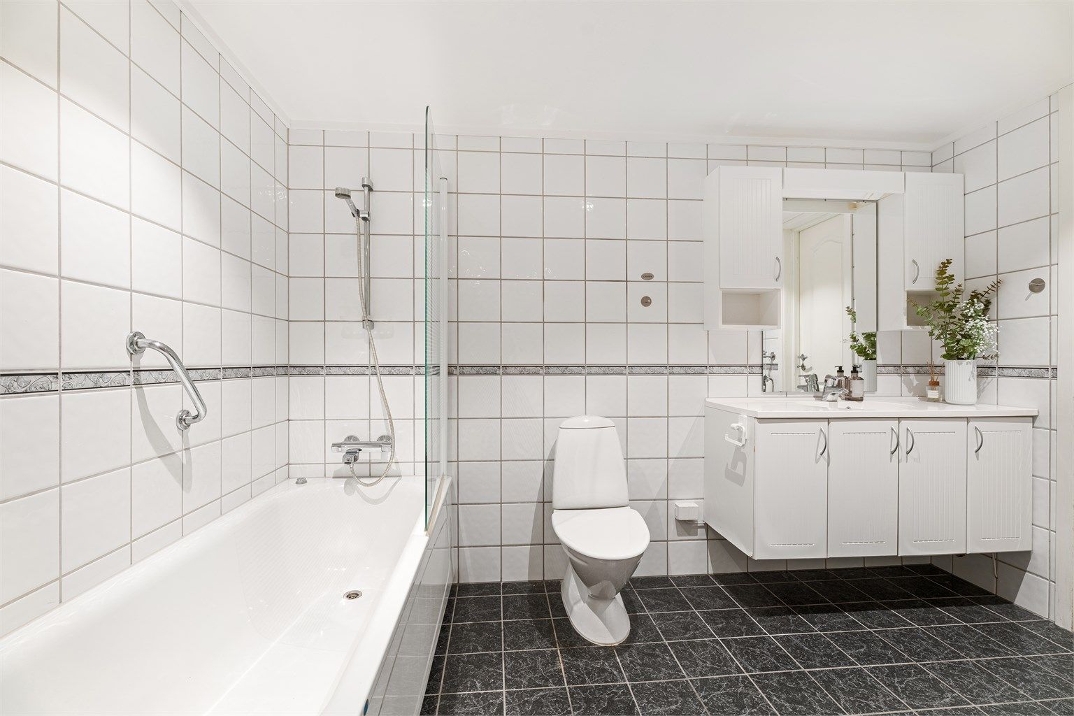 Videre er det stående toalett samt badekar med dusjvegg. 