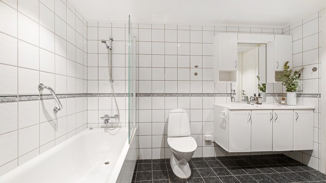 Videre er det stående toalett samt badekar med dusjvegg.