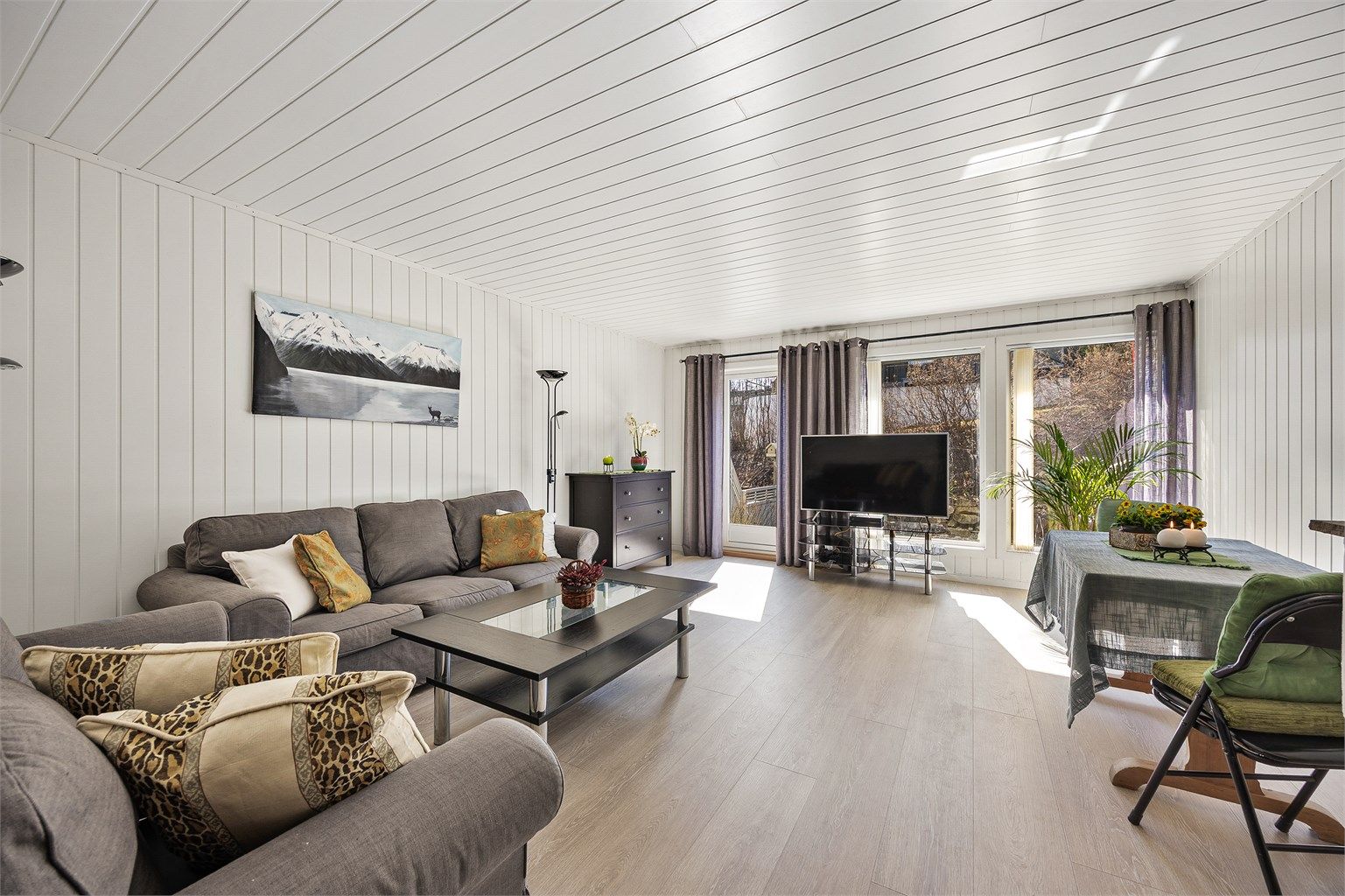 Stuen har plass til både sofagruppe og spisebord, med overflater som inkluderer laminatgulv og panel på veggene.