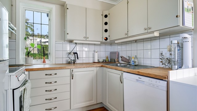 Kjøkkeninnredning med heltre benkeplate og avsatt plass til oppvaskmaskin og komfyr.