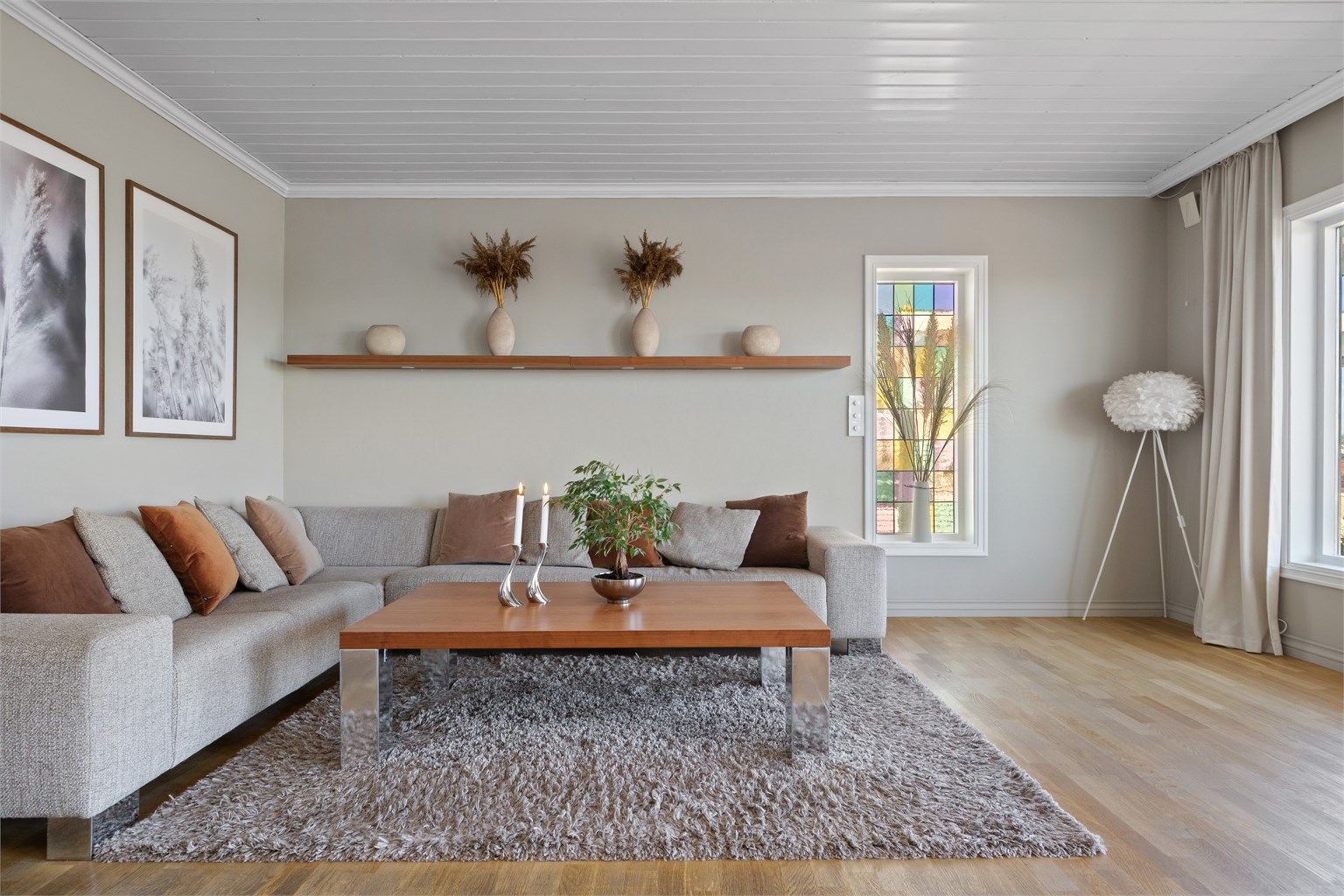 Stuen har parkettgulv, lysbeige, glatte veggflater og hvitmalt panelhimling med bjelker.