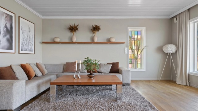 Stuen har parkettgulv, lysbeige, glatte veggflater og hvitmalt panelhimling med bjelker.