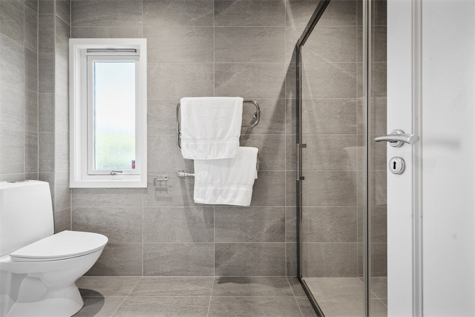 Badet er innredet med vegghengt servantinnredning med ovenpåliggende servant, speilskap med overlys og stikkontakt, dusjnisje med glassdører samt gulvstående toalett. 