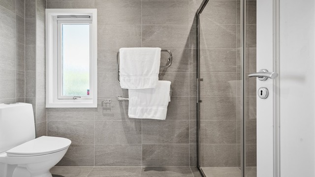 Badet er innredet med vegghengt servantinnredning med ovenpåliggende servant, speilskap med overlys og stikkontakt, dusjnisje med glassdører samt gulvstående toalett.