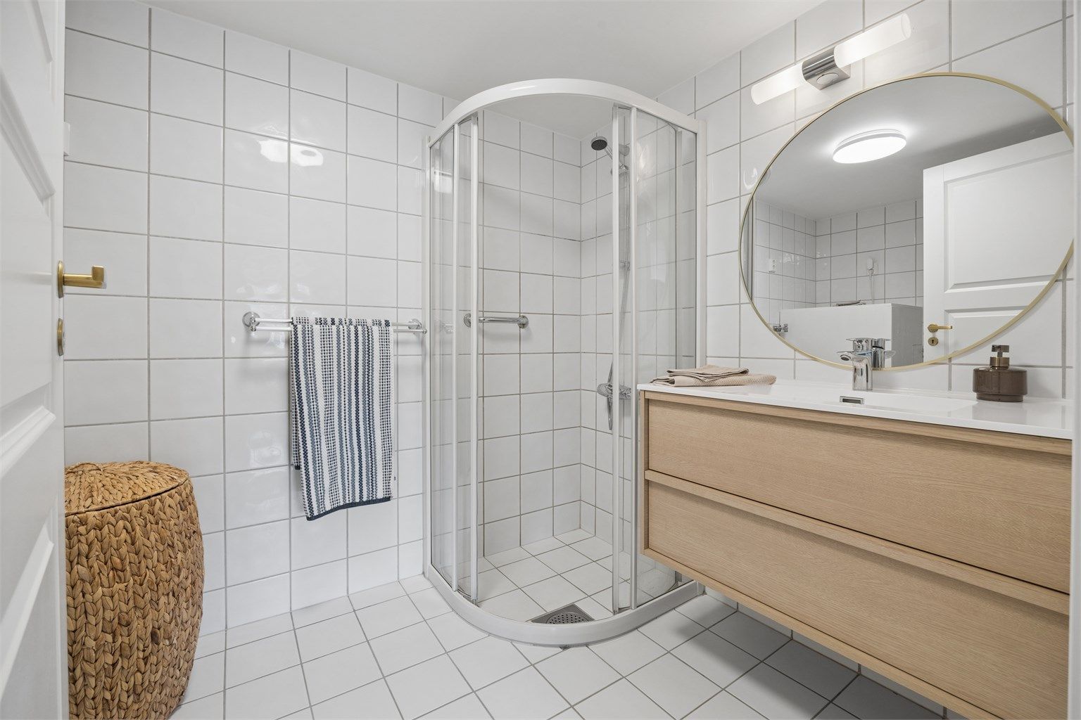 Badet har flislagte overflater, gulvvarme og et praktisk dusjhjørne med skyvedørsramme.