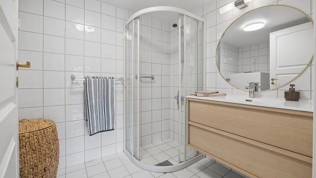 Badet har flislagte overflater, gulvvarme og et praktisk dusjhjørne med skyvedørsramme.
