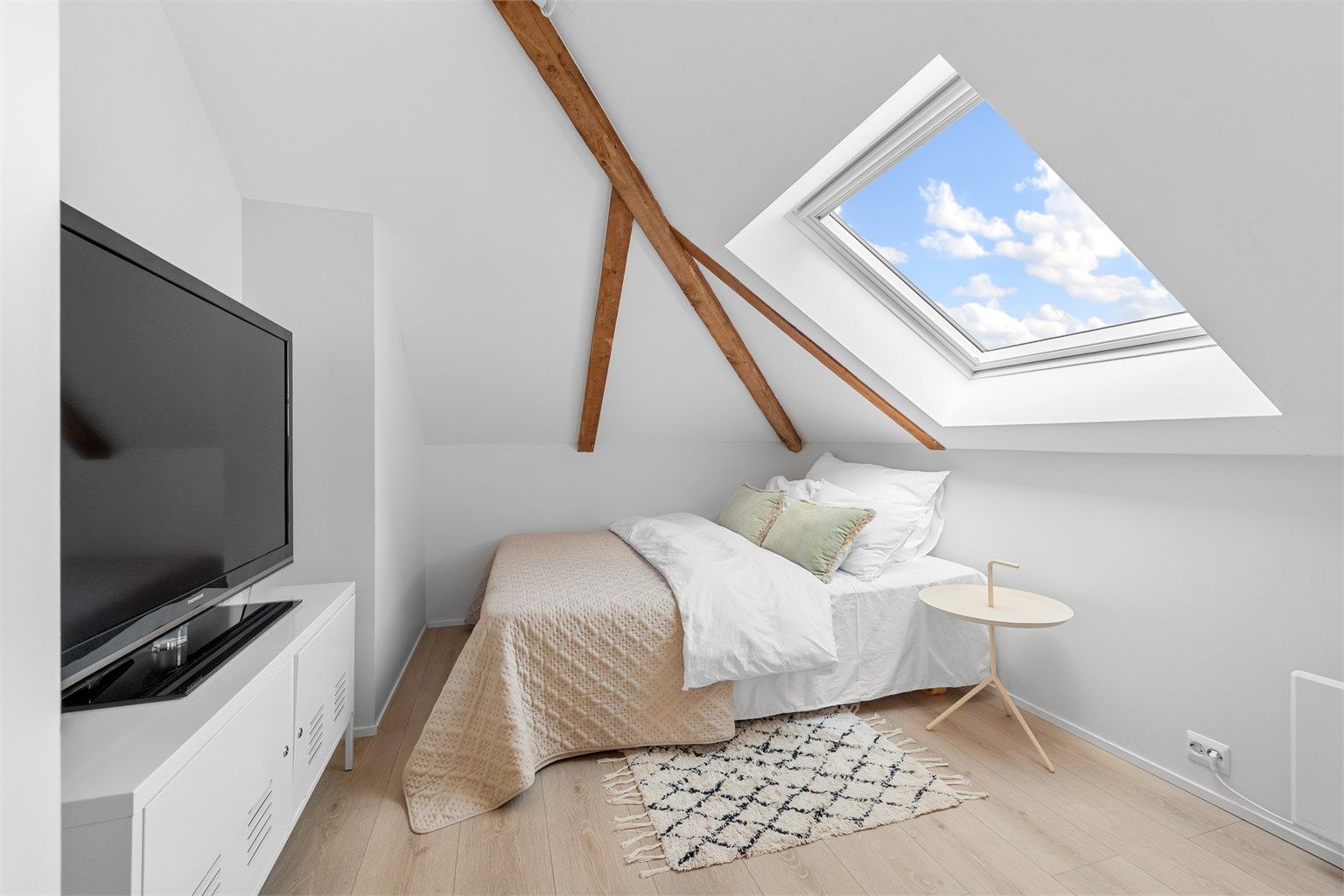 Rommet har plass til seng og oppbevaringsløsninger, med et takvindu som gir naturlig lys.