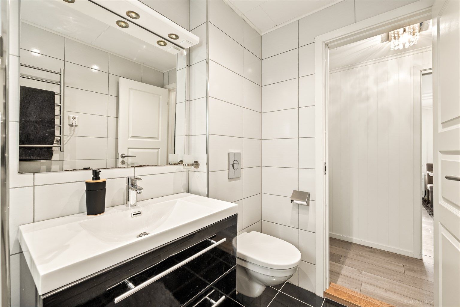 Her er det vegghengt toalett, servantinnredning og speil med overlys.