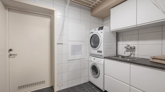 Praktisk vaskerom fra byggeår med benkeplass, oppbevaring, utslagsvask og opplegg for vaskemaskin og tørketrommel.