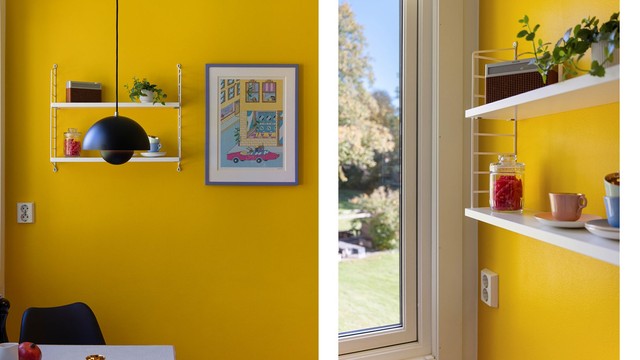 Gjennomtenkte detaljer gir kjøkkenet sjel. Lette, åpne hyller mot den gule veggen gir rom for planter og pent servise, mens vinduet slipper inn rikelig med dagslys og byr på utsyn mot grønne omgivelser.
