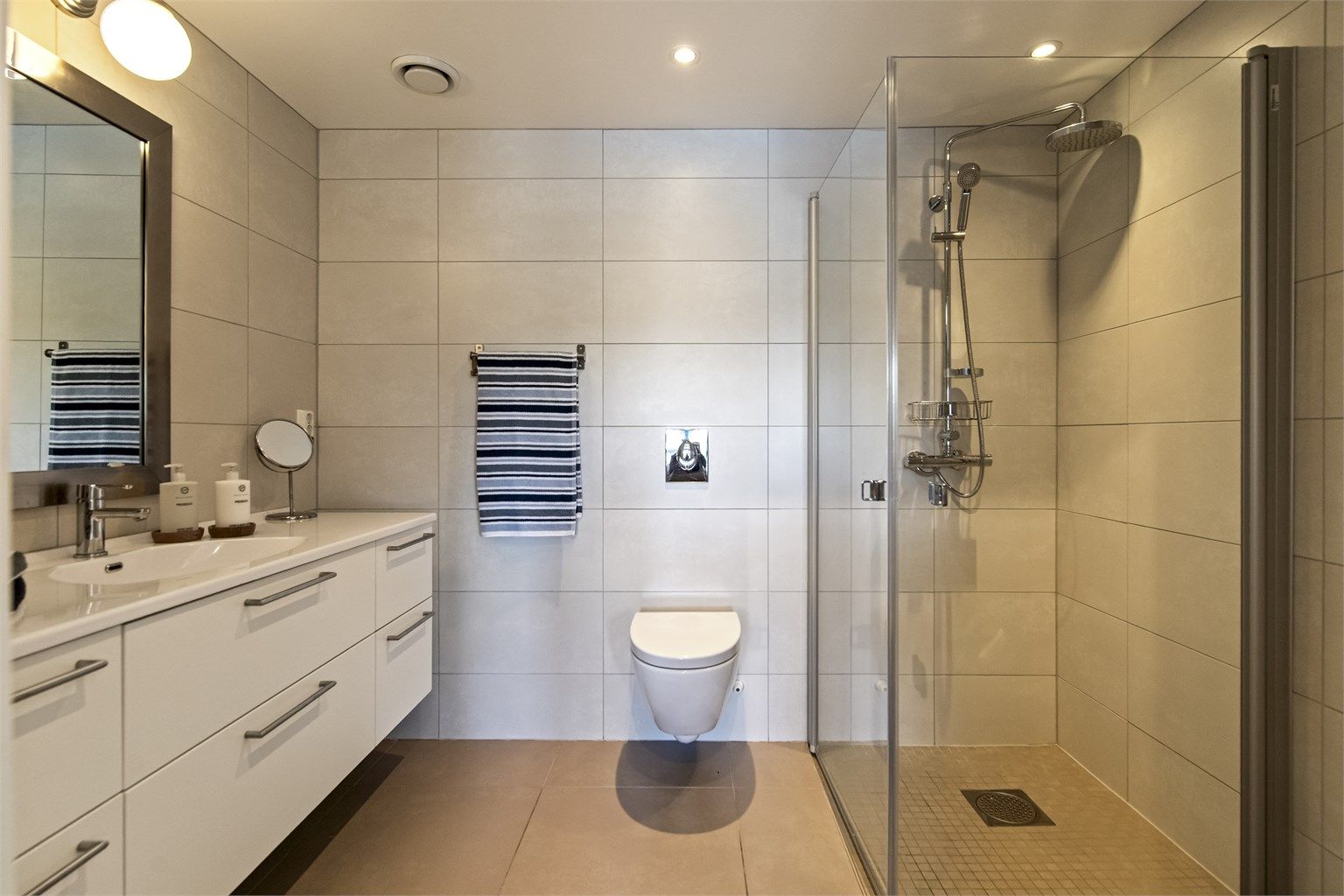 Hovedbadet, har adkomst fra hovedsoverommet, er romslig med flislagt gulv med varme, downlights i taket og vegghengt toalett. 