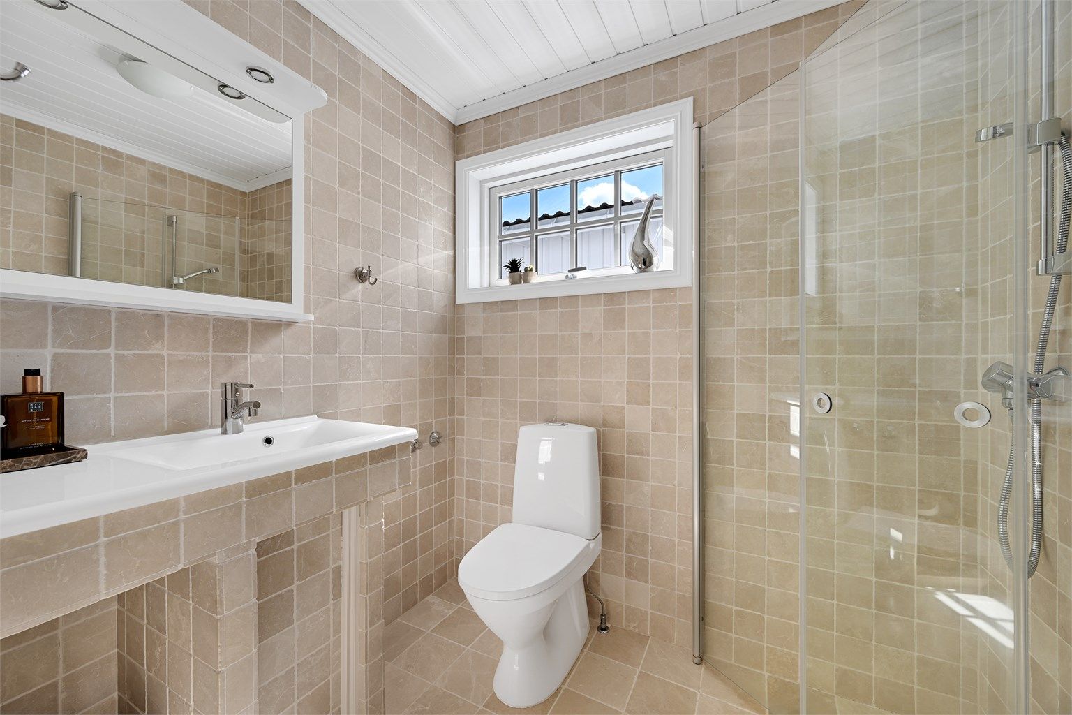 Badet er stilrent og flislagt med varmekabler i gulvet, og er utstyrt med toalett, dusjløsning, servant med baderomsinnredning. 