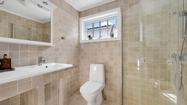 Badet er stilrent og flislagt med varmekabler i gulvet, og er utstyrt med toalett, dusjløsning, servant med baderomsinnredning.
