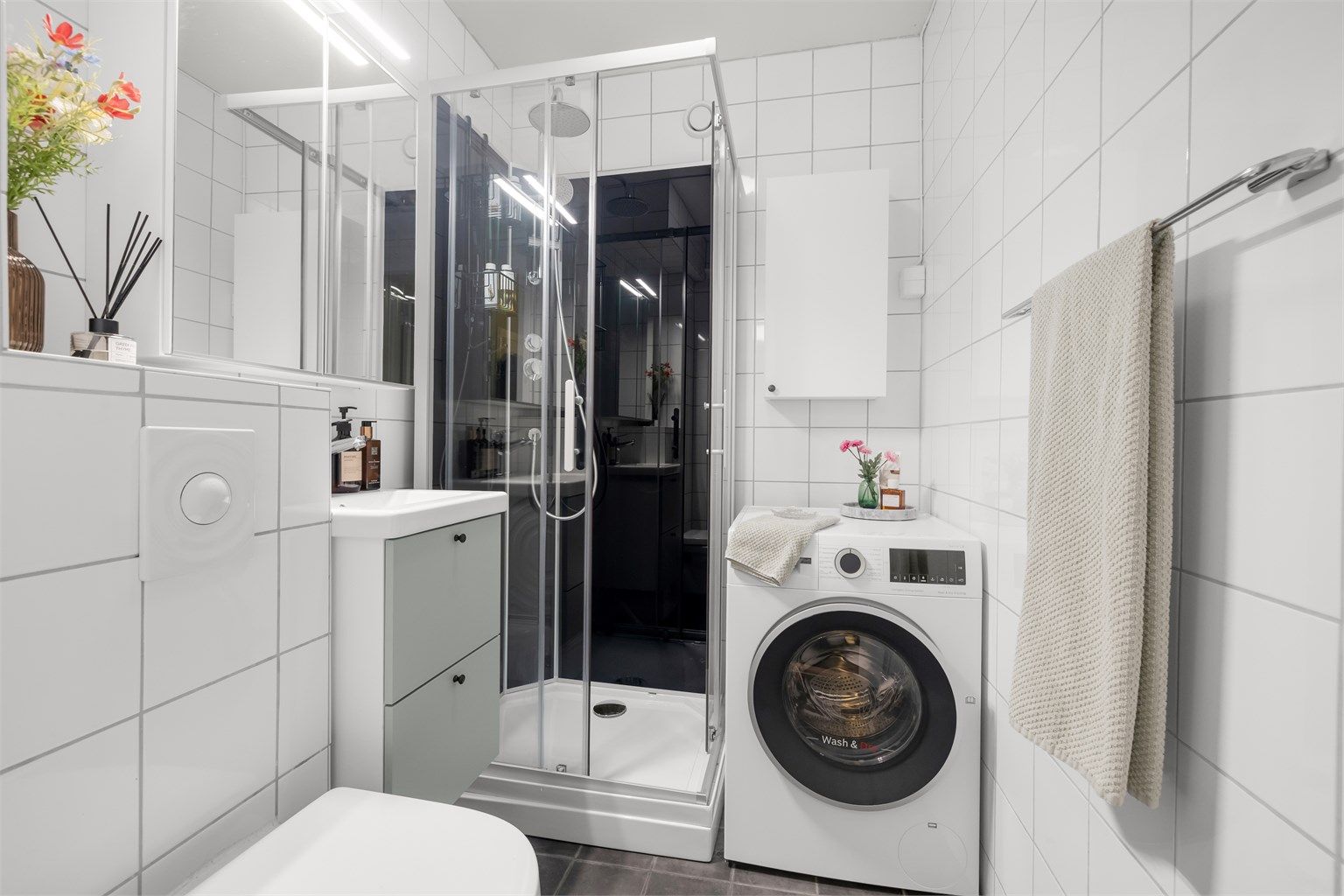 Badet har fliser på vegger og gulv, med komfortabel elektrisk gulvvarme. Her er det dusjkabinett og praktisk opplegg for vaskemaskin.
