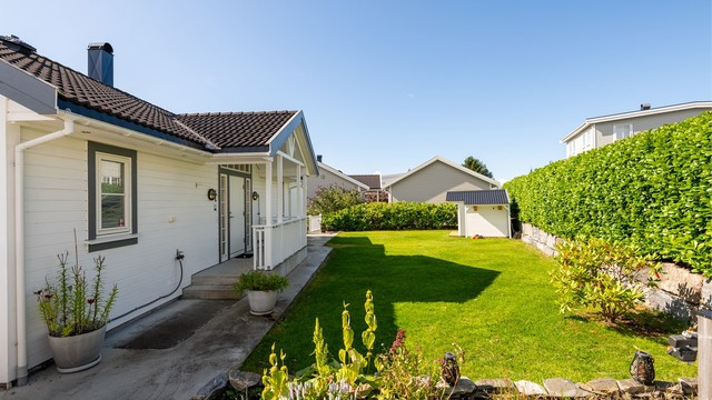 Inngangsparti med støpt gangsti langs husveggen og frodige beplantninger.