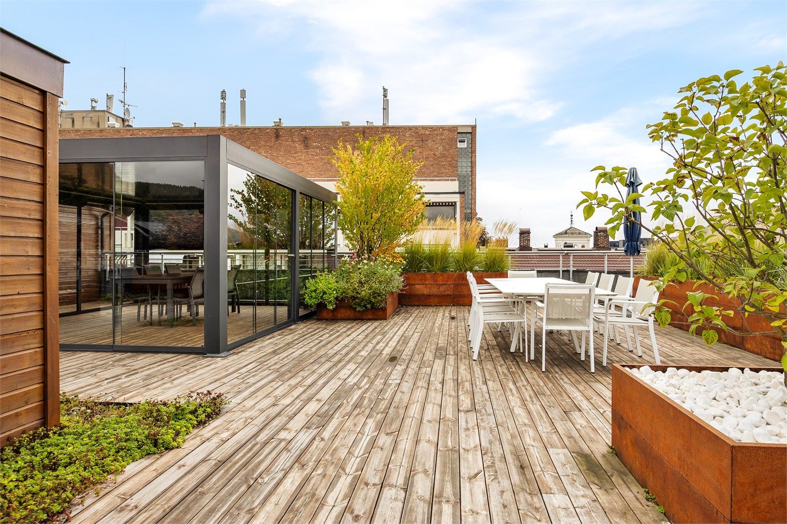 Felles takterrasse med innglasset pergola, sittegrupper og frodig beplantning.