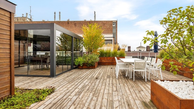 Felles takterrasse med innglasset pergola, sittegrupper og frodig beplantning.