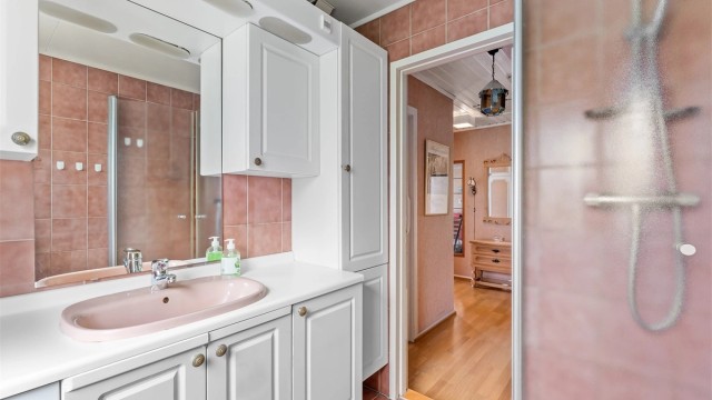 Badet i første etasje har flislagte overflater og dusjhjørne med innfellbare glassdører.