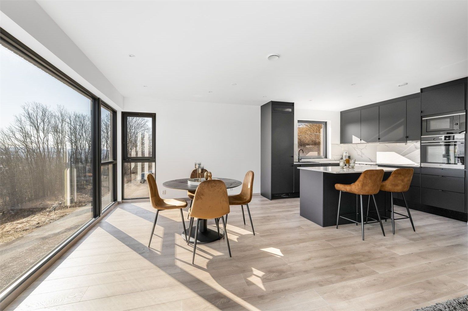 Kjøkkendelen har en pen takhøy innredning fra Systemkjøkken med sorte slette fronter, laminert benkeplate med stålvask og Kitchen Wall plater over kjøkkenbenk.