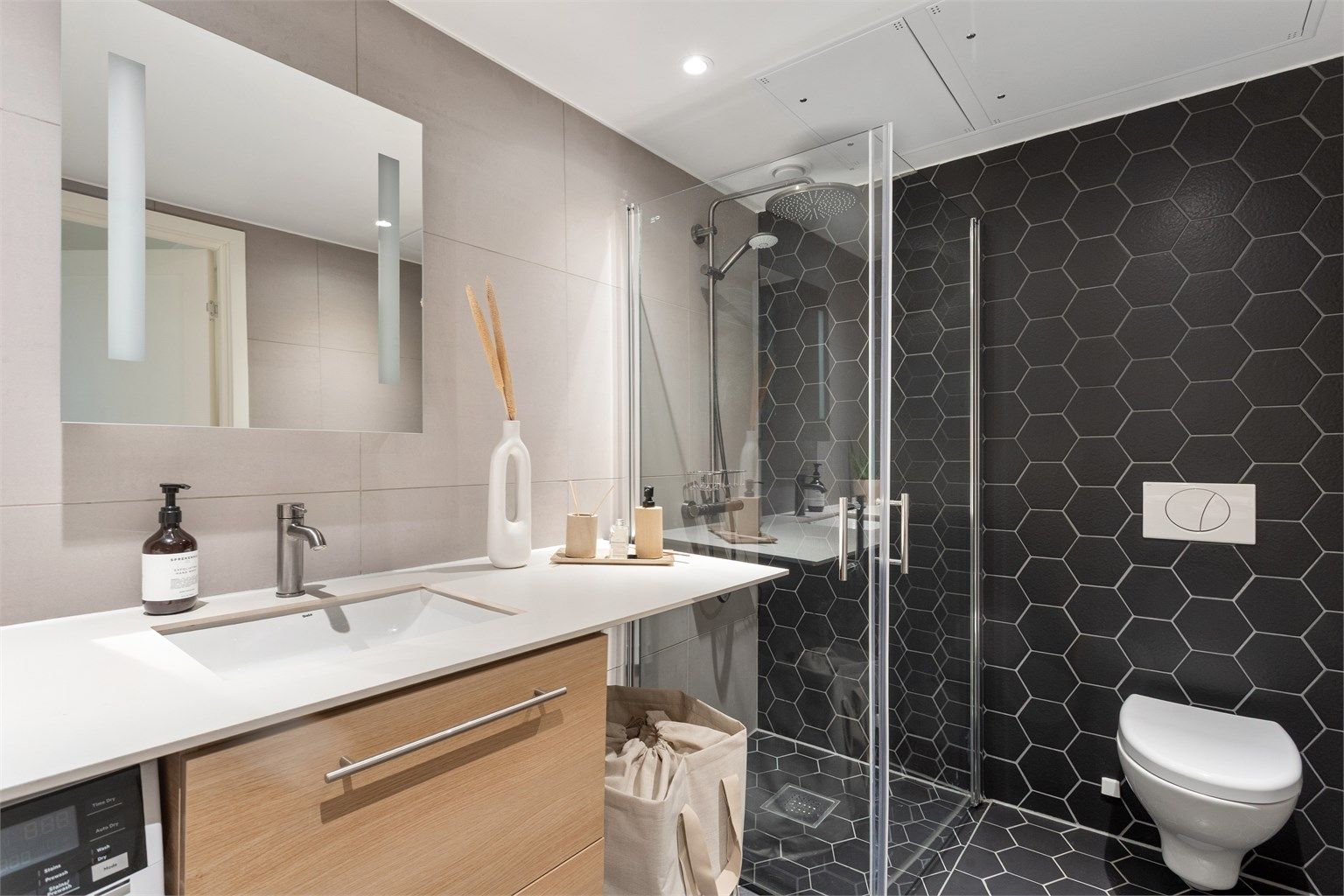 Delikat, flislagt bad med elektrisk gulvvarme, vegghengt toalett og et romslig dusjhjørne med svingbare glassdører.