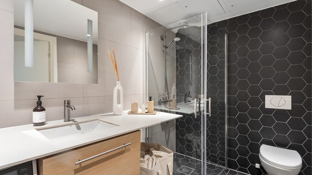 Delikat, flislagt bad med elektrisk gulvvarme, vegghengt toalett og et romslig dusjhjørne med svingbare glassdører.