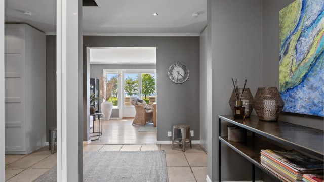 Entreen glir sømløst over i en hall med downlights i taket, innredet med samme type skap og overflater.