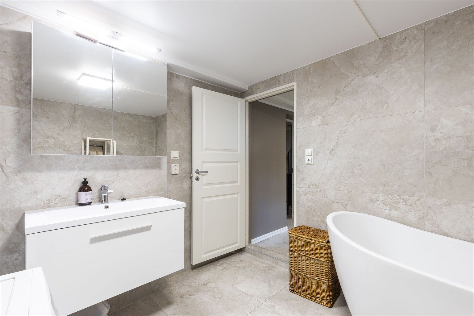 Bad i kjeller fra 2023/2024. Gulv og veggflater belagt med flis. Himling med malt slett flate. Innredning med slett skuffefront, heldekkende servant og speilskap med overlys. Varmekabler i gulv. 