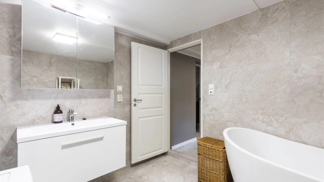 Bad i kjeller fra 2023/2024. Gulv og veggflater belagt med flis. Himling med malt slett flate. Innredning med slett skuffefront, heldekkende servant og speilskap med overlys. Varmekabler i gulv.