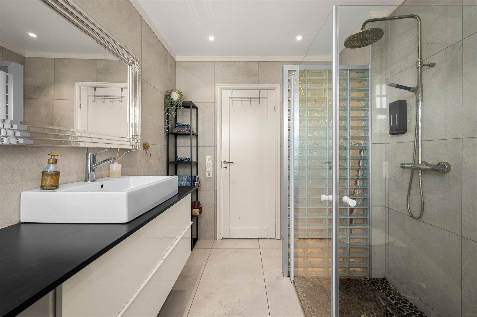 Badet har en romslig dusjsone med både hånd- og takdusj, samt moderne og tidløse flisvalg.