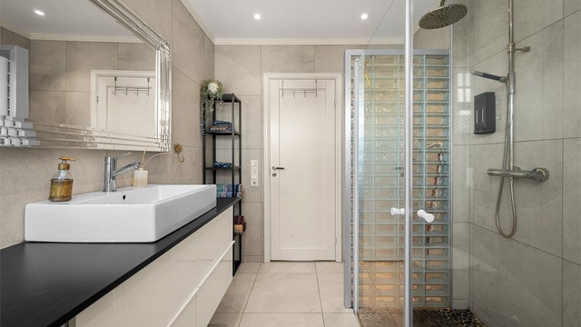 Badet har en romslig dusjsone med både hånd- og takdusj, samt moderne og tidløse flisvalg.