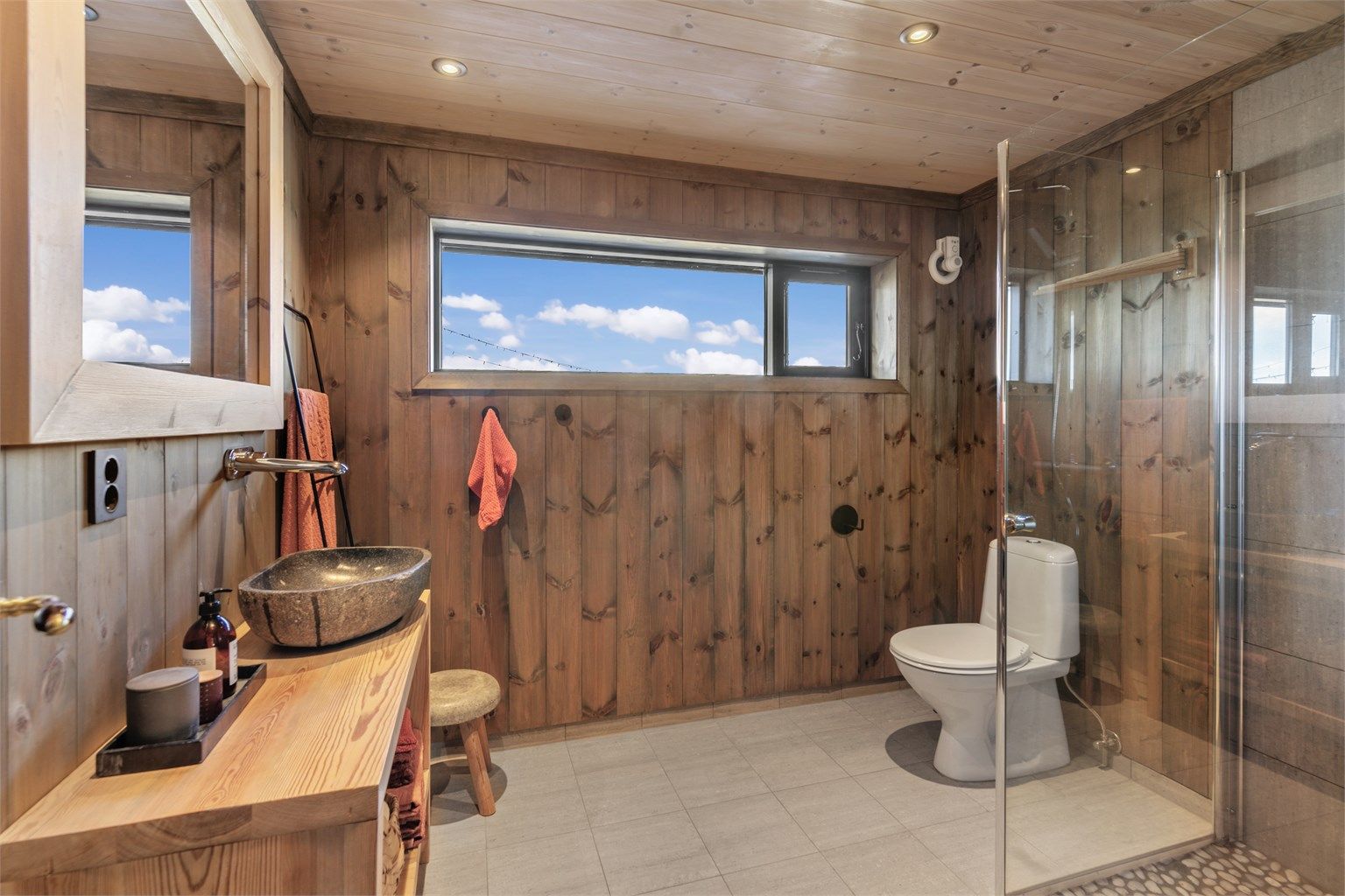 Badet har flislagt gulv med gulvvarme, innredning i tre og en toppmontert servant.