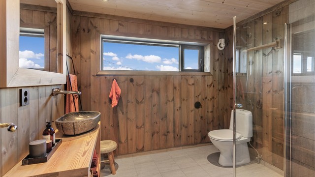 Badet har flislagt gulv med gulvvarme, innredning i tre og en toppmontert servant.