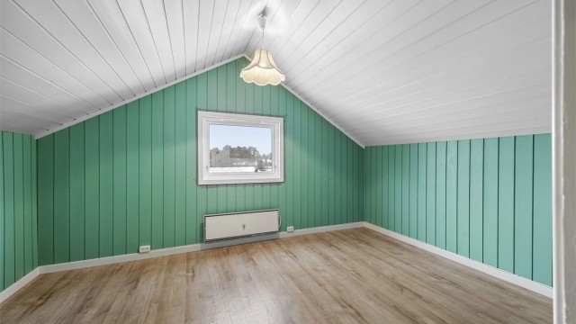 Det ene av to innredede rom på loftet, med panel på vegger og i skråtak.