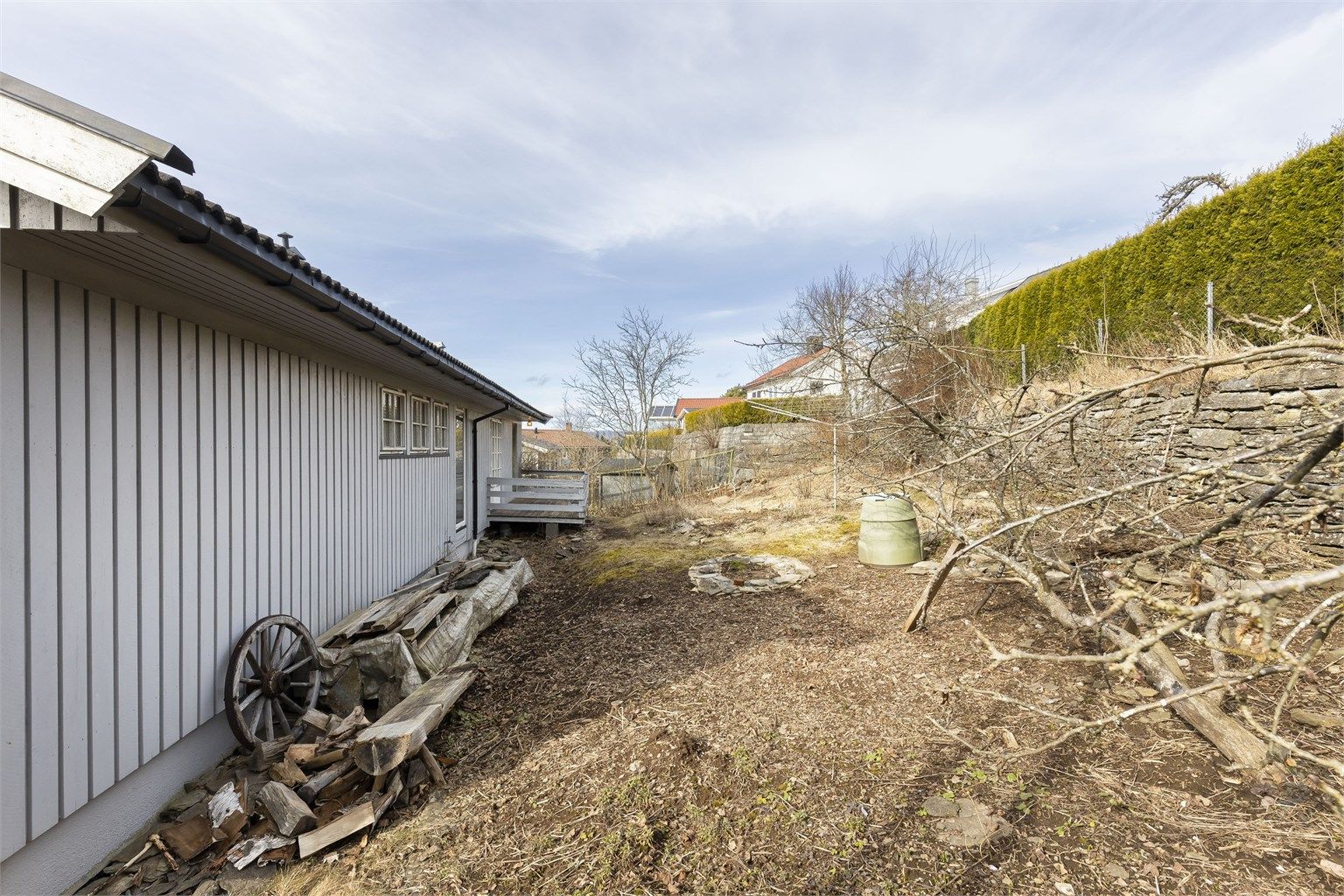 Usjenert hage på husets bakside med stenmur og diverse beplantning. 