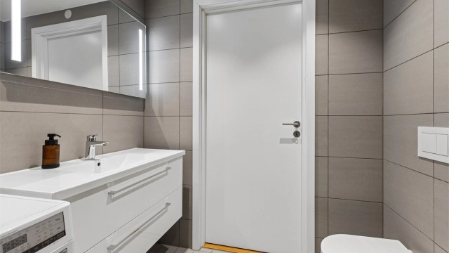 Lekkert flislagt bad med gulvvarme. Her finnes dusjhjørne med innfellbare glassdører, moderne servantinnredning, vegghengt toalett og opplegg for vaskemaskin.