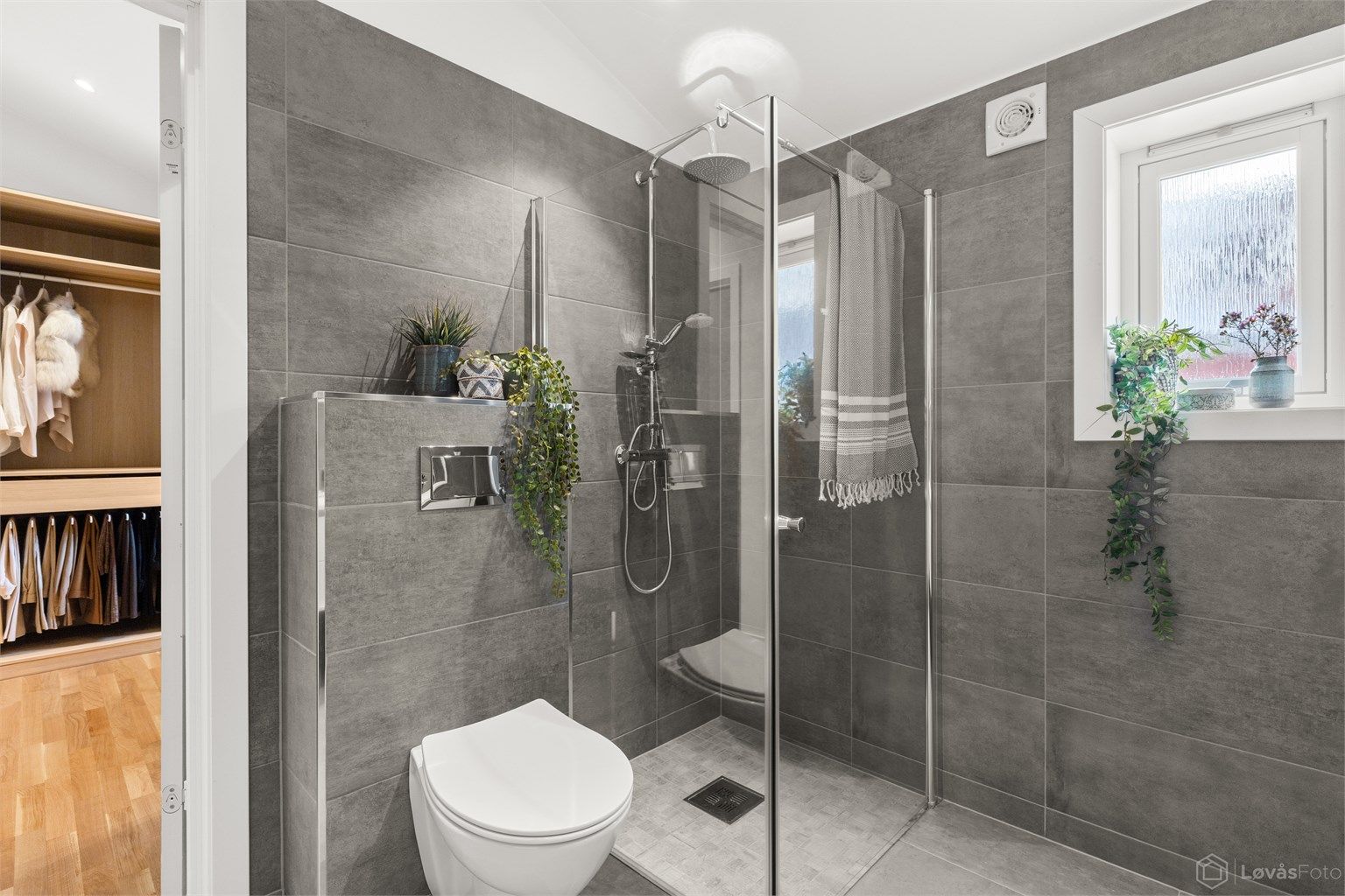 Badet er utstyrt med dusjhjørne med glassvegger, regnfalldusj og vegghengt toalett.