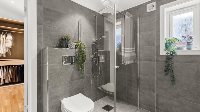 Badet er utstyrt med dusjhjørne med glassvegger, regnfalldusj og vegghengt toalett.